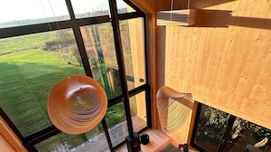 Un interior moderno con ventanas amplias, piso de madera, un sofá, una mesa y lámparas colgantes.