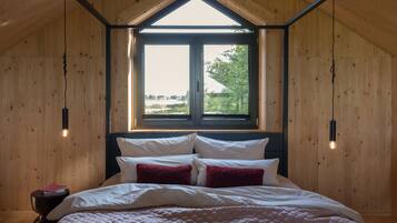 Ein Schlafzimmer mit Holzboden, einem großen Fenster und einem Bett mit weißen und roten Kissen.