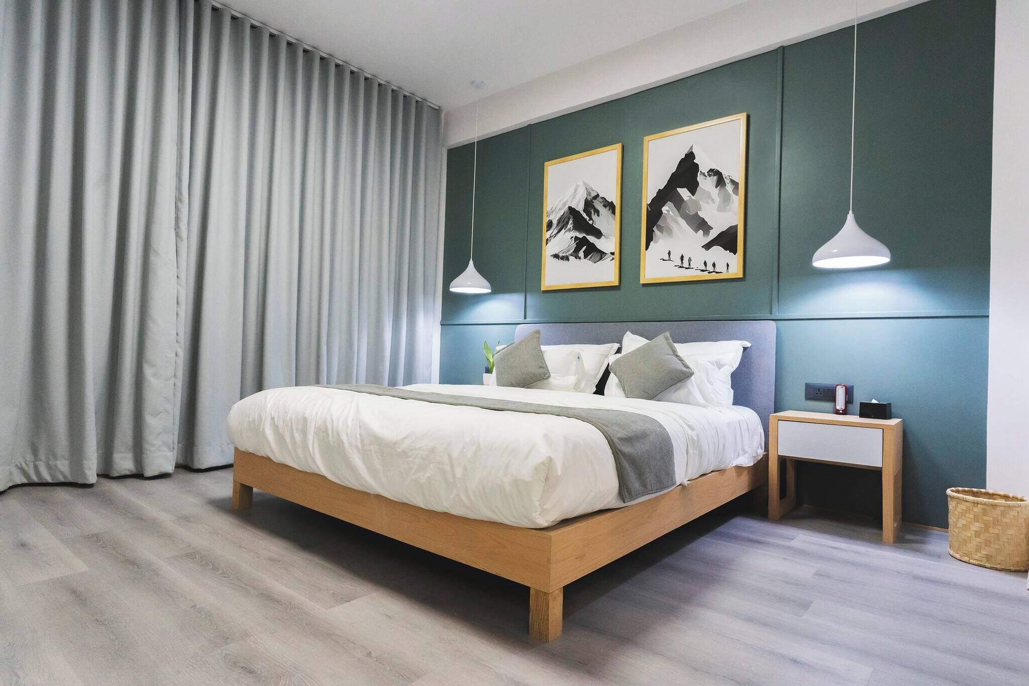 A modern bedroom with a wooden bed, grey curtains, and two framed mountain art pieces on the wall.