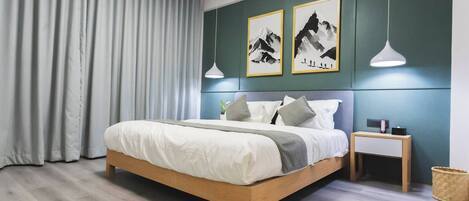 A modern bedroom with a wooden bed, grey curtains, and two framed mountain art pieces on the wall.