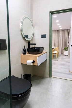 A modern bathroom with a black toilet, a wooden vanity with a black sink, a mirror, and a toilet paper holder. - Modern 2 Bedroom Apartment in Putalisadak, Kathmandu (Kathmandu)