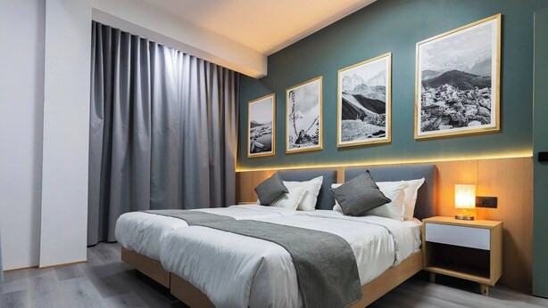 Una camera da letto moderna con un letto grande, tende grigie e tre quadri in bianco e nero raffiguranti paesaggi.