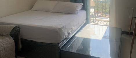 A hotel room with a bed, a ceiling fan, a clock, a view of the outside, and a balcony.