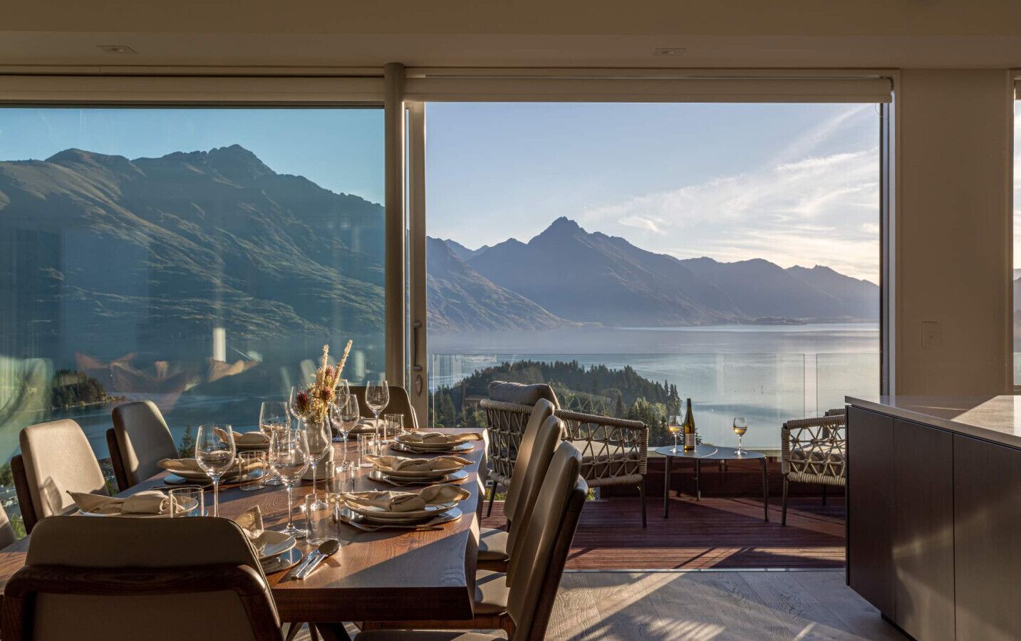 A dining area with a table set for four, overlooking a lake and mountains.