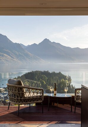 A terrace with wicker chairs and a table, overlooking a mountainous landscape and a body of water. - Atanga | Showstopper Views | Spa Pool (Queenstown)