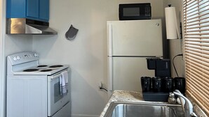 A compact kitchen with white appliances, blue cabinets, and a stainless steel sink.