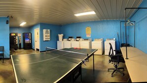 A room with a foosball table, ping pong table, and a bench. There are cabinets and a mop rack.