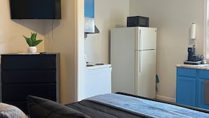 A bedroom with a bed, a dresser, a flat-screen TV, a microwave, and a refrigerator.