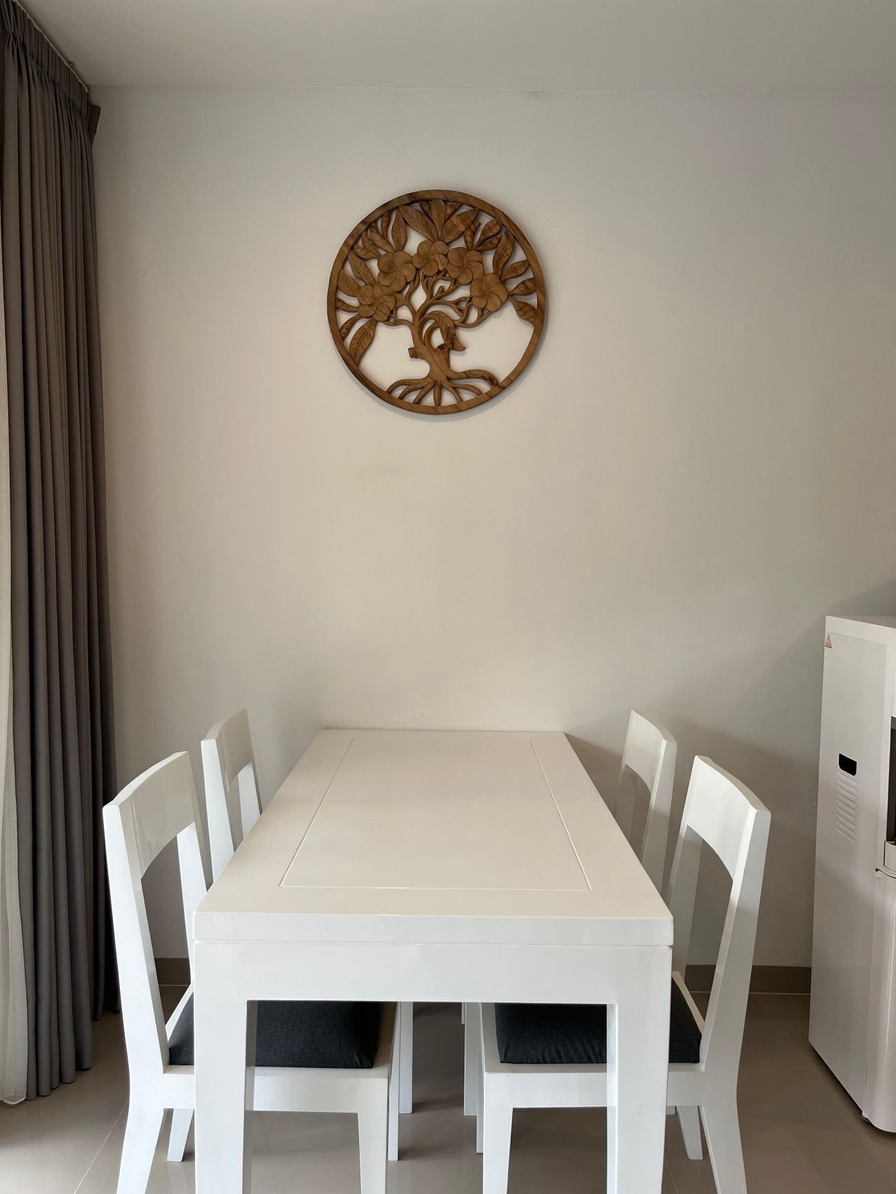 Ein Essbereich mit einem weißen Tisch und Stühlen, einem dekorativen Holzgegenstand an der Wand und einem weißen Kühlschrank.