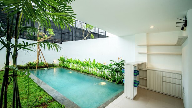 Ein moderner Poolbereich im Innenbereich mit freiem Blick zum Himmel, umgeben von üppiger Vegetation und einem minimalistischen Design.