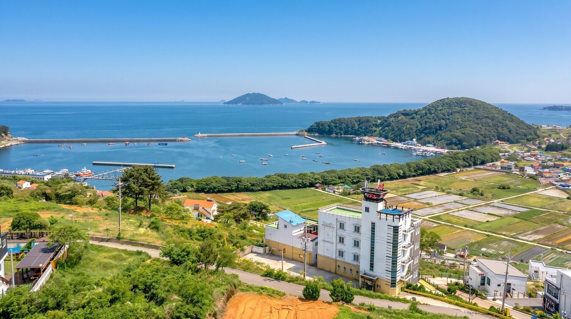 A coastal town with a marina, residential buildings, and agricultural fields.