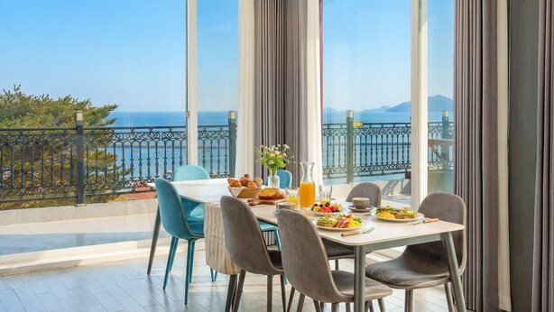 A dining area with a table set for breakfast, overlooking a scenic view of the sea and mountains. - Namhae Onview Pension (Namhae)