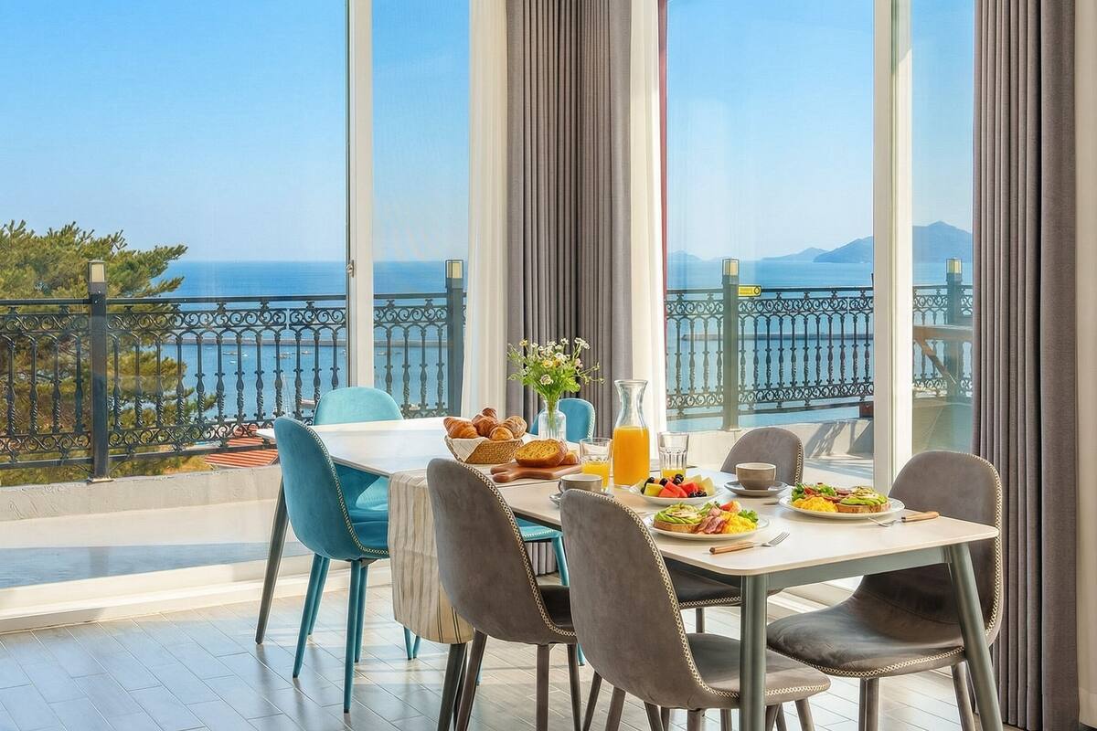Un comedor con una mesa dispuesta para el desayuno, con vistas panorámicas al mar y las montañas.