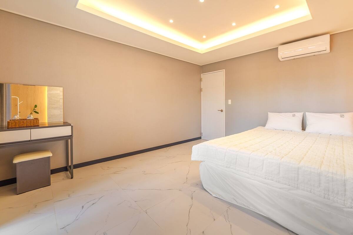 Un dormitorio con cama, escritorio, silla, espejo y unidad de aire acondicionado.