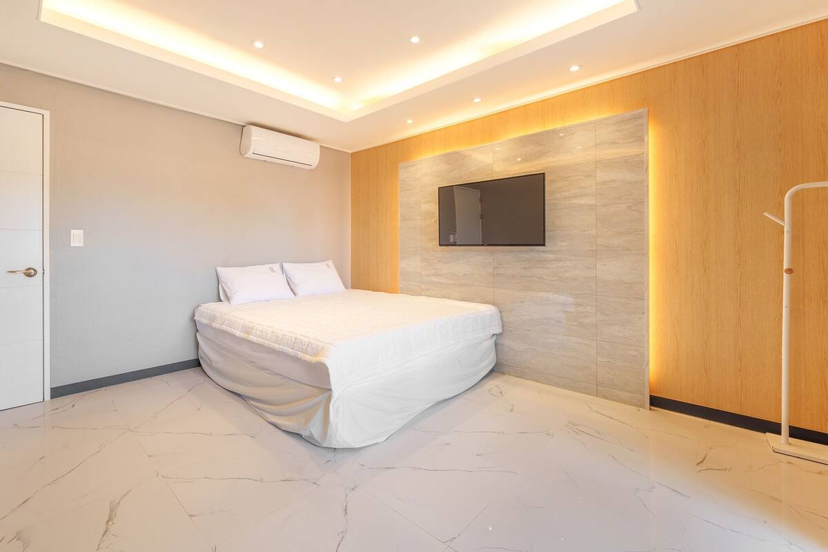 Un dormitorio moderno con cama, televisión montada en la pared y un panel de madera.