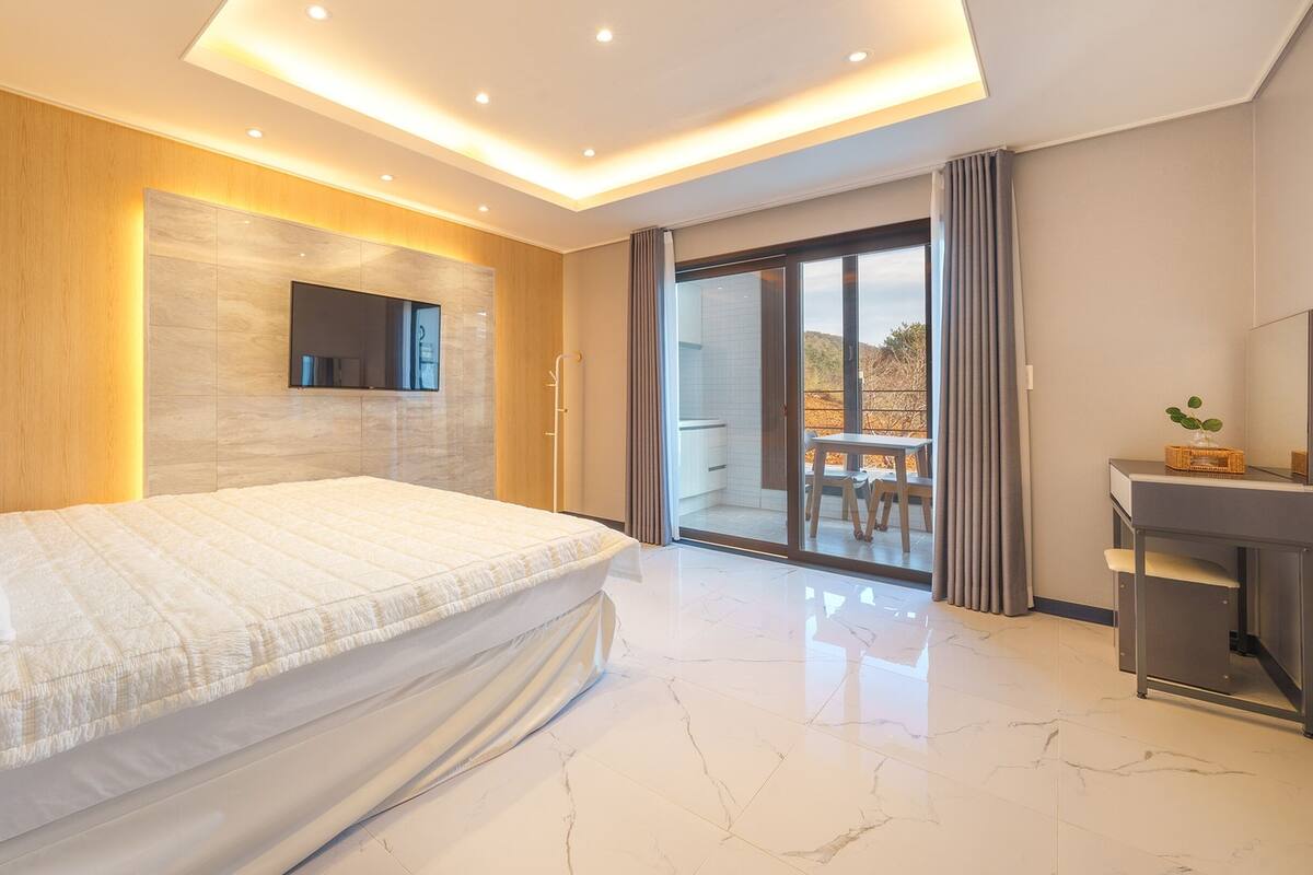 Un dormitorio moderno con una cama grande, un televisor montado en la pared y un ventanal corredero que da a un balcón.