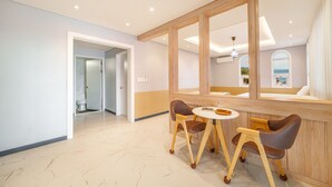 A hotel room with a wooden-framed mirror, a round table with two chairs, a bed with a view of the sea, and a bathroom with a toilet and shower. - Namhae Onview Pension (Namhae)