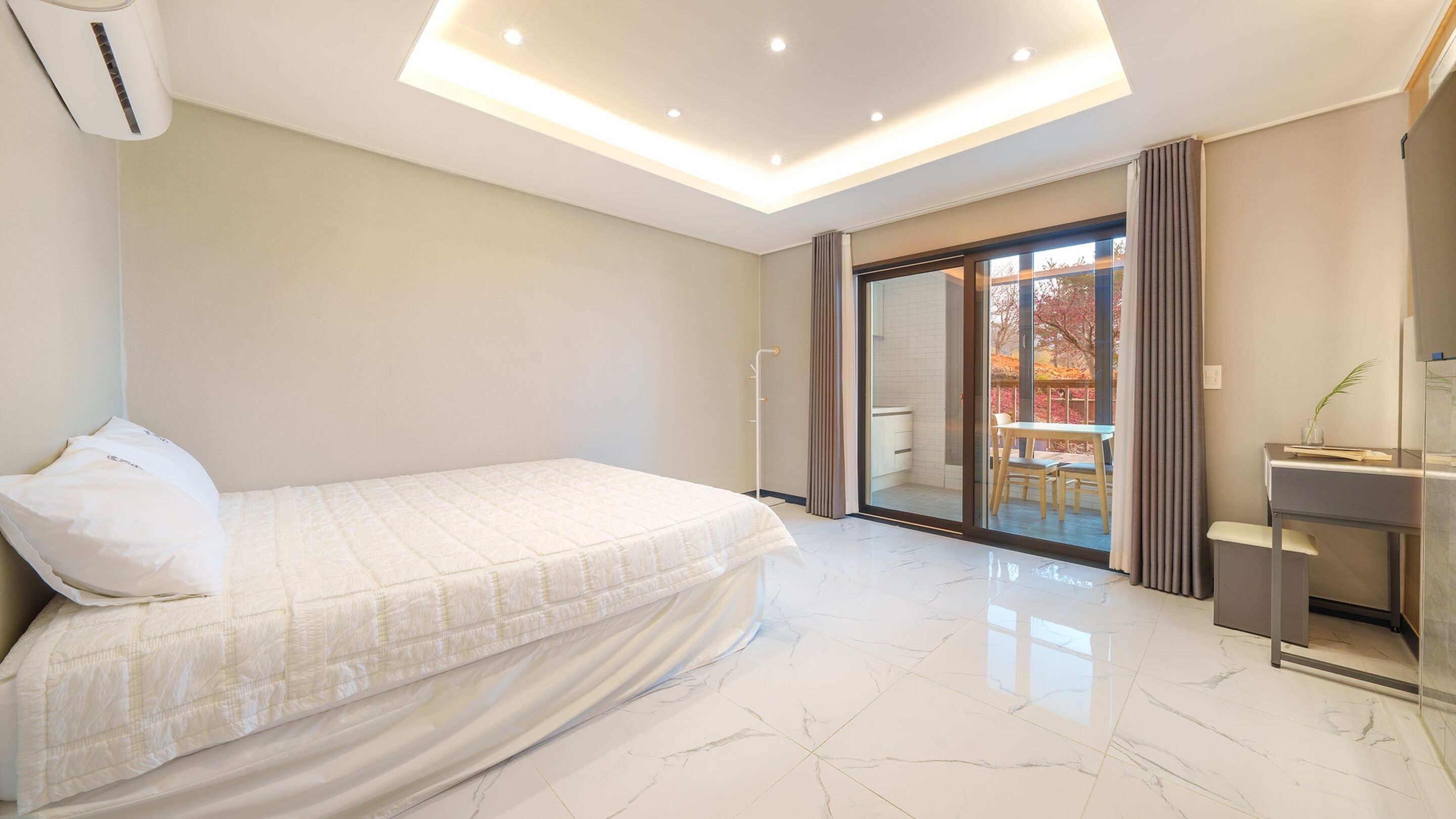 A modern bedroom with a bed, a desk, and a sliding glass door leading to a balcony.