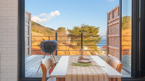 Un comedor con mesa y sillas, una parrilla y vistas al mar y las colinas.