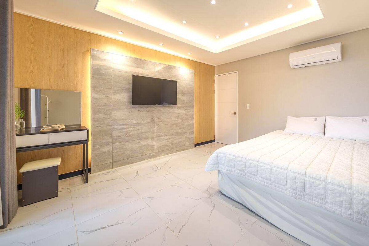 Un dormitorio moderno con una cama, un escritorio y un televisor montado en la pared.