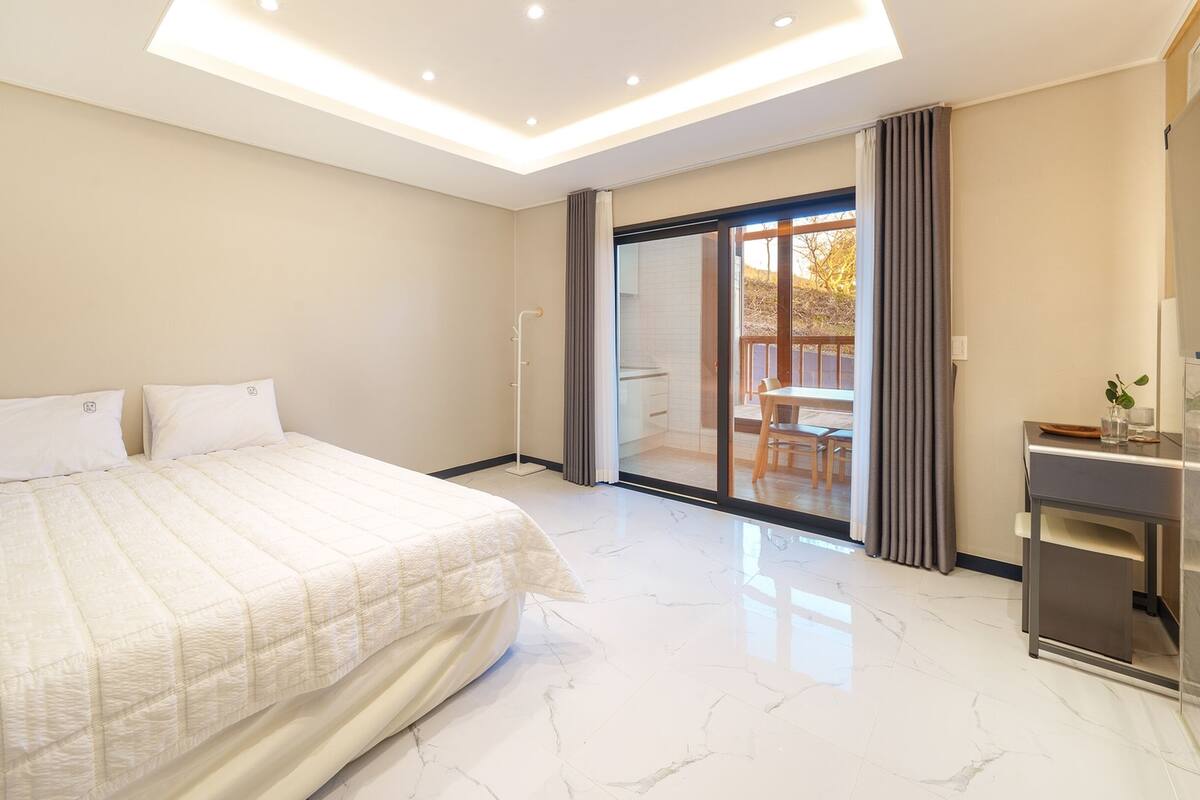 Un dormitorio moderno con una cama grande, un escritorio y un ventanal corredera que da a un balcón.