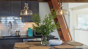 Une cuisine avec un îlot central en bois, un vase contenant des plantes vertes et des suspensions lumineuses.