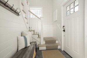 Una escalera que lleva a una puerta, un banco con cojines y un perchero en la pared.