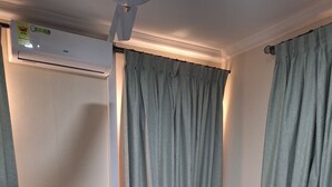 Een hotelkamer met een bed, gordijnen, een airconditioning en een bedieningspaneel.