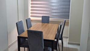Een eetruimte met een houten tafel, zes stoelen, een raam met jaloezieën en een plafondlamp.