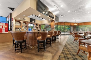 A bar area with a counter, stools, and a view through large windows.