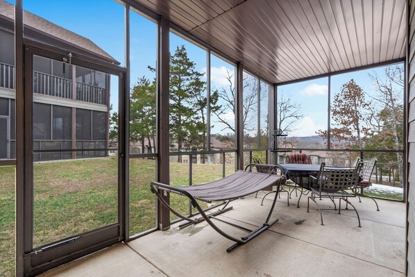A covered patio with a table and chairs, a hammock, and a view of a backyard and trees. - Townhouse at Stonebridge Near Silver Dollar City_Free Tickets _Golf Course_Outdoor Pool (Branson West)