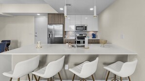 A modern kitchen with white cabinetry, stainless steel appliances, and a central island with bar stools.