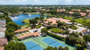 A tennis court surrounded by lush greenery and a lake.
