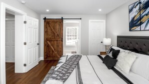 A bedroom with a bed, a wooden sliding door, a white door, a lamp, and a painting on the wall.