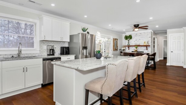 A modern kitchen with white cabinets, a stainless steel refrigerator, and a marble island with bar stools.