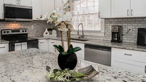 A kitchen with white cabinets, a granite countertop, a black microwave, a stove, and a sink.