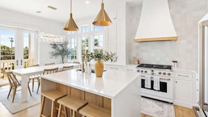 Une cuisine moderne dotée d’un grand îlot central, de luminaires suspendus et offrant une vue sur l’extérieur.