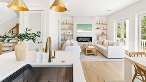 Un salon moderne avec un canapé blanc, une table basse et un téléviseur. On y trouve également un coin cuisine avec un évier et un vase rempli de plantes.