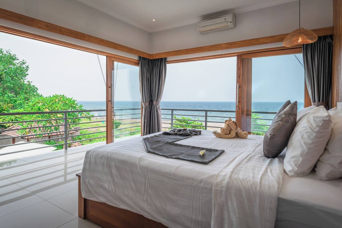 A bedroom with a large bed, a view of the ocean, and a balcony with a railing.