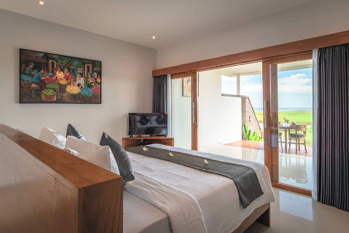 A bedroom with a large bed, a TV, and a balcony with a view of the landscape.
