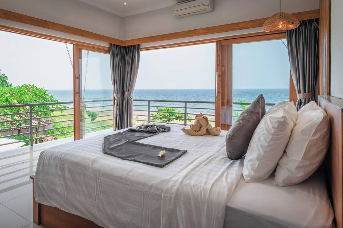 A bedroom with a large bed, a view of the sea, and a balcony with a railing.