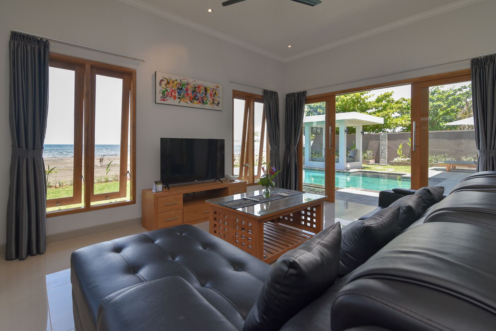 A modern living room with a large black leather sofa, a flat-screen TV on a wooden stand, and a glass coffee table.