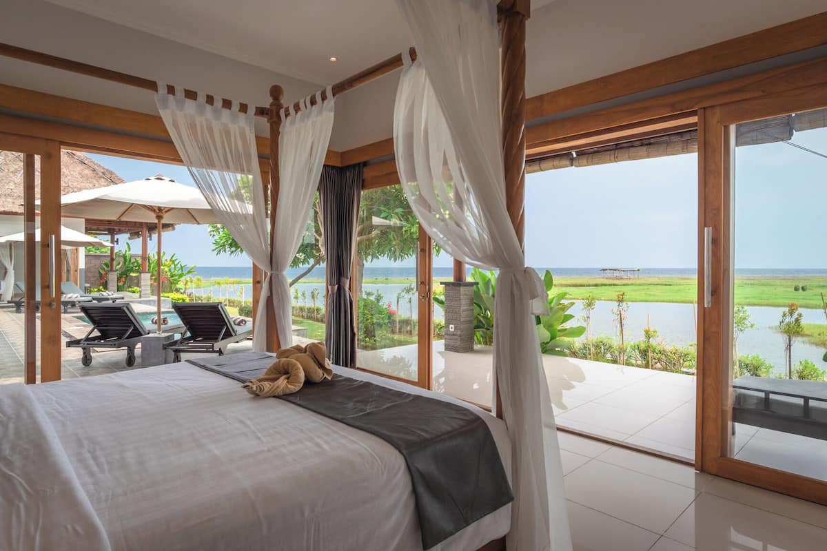 A bedroom with a large bed, a view of a lake, and a pool area with lounge chairs.