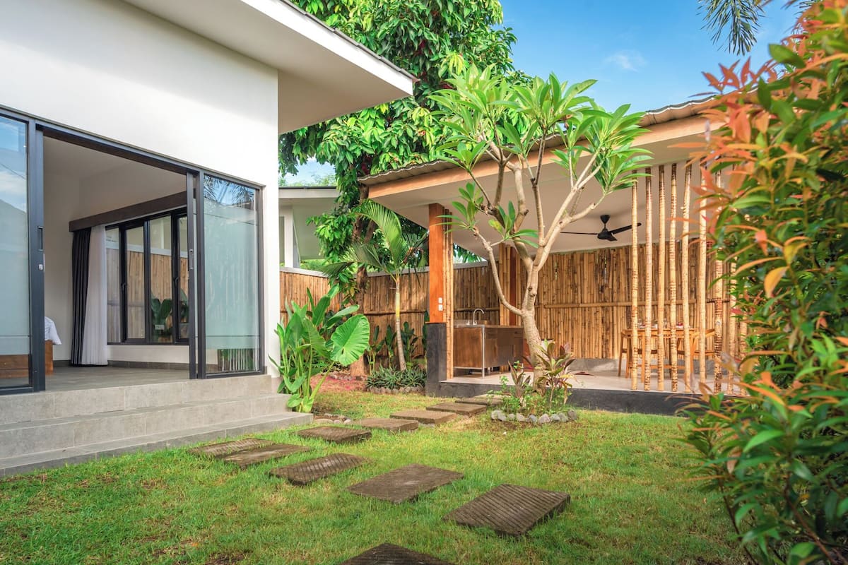A modern house with a glass door entrance, a covered outdoor kitchen, and a bamboo fence.