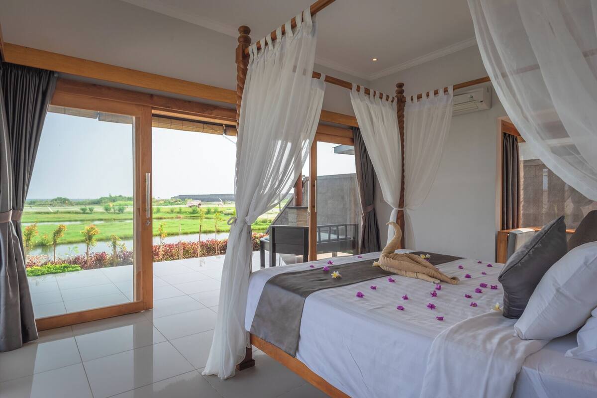 A four-poster bed with a view of a green landscape through large windows.