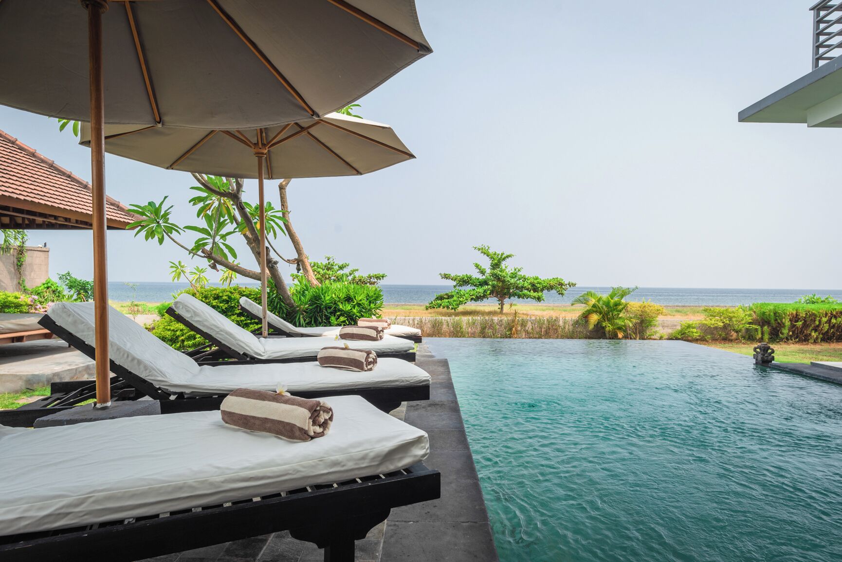 A poolside area with lounge chairs and umbrellas, overlooking a beach and ocean.