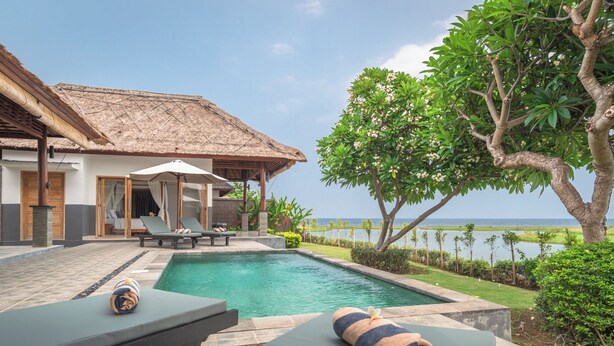 A poolside area with a thatched-roof structure, lounge chairs, and a view of the sea. - The Manik Kalisada (Seririt)