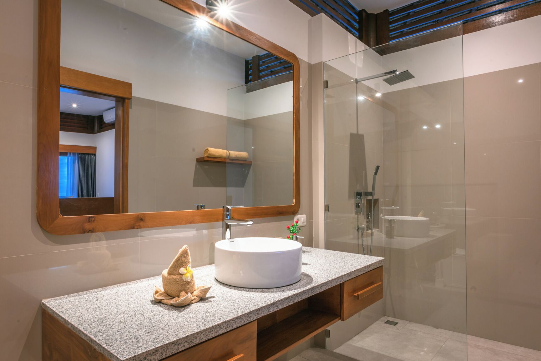 A modern bathroom with a granite countertop, a round sink, a large mirror, and a glass-enclosed shower area.