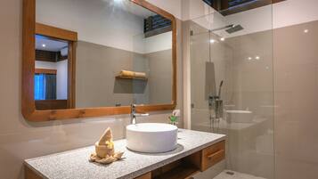 A modern bathroom with a granite countertop, a round sink, a large mirror, and a glass-enclosed shower area.