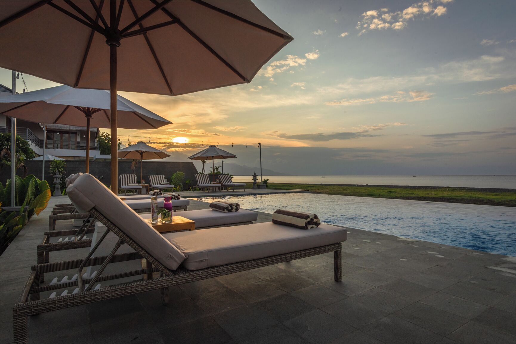 Ein Poolbereich mit Liegestühlen, Sonnenschirmen und Blick auf das Meer bei Sonnenuntergang.